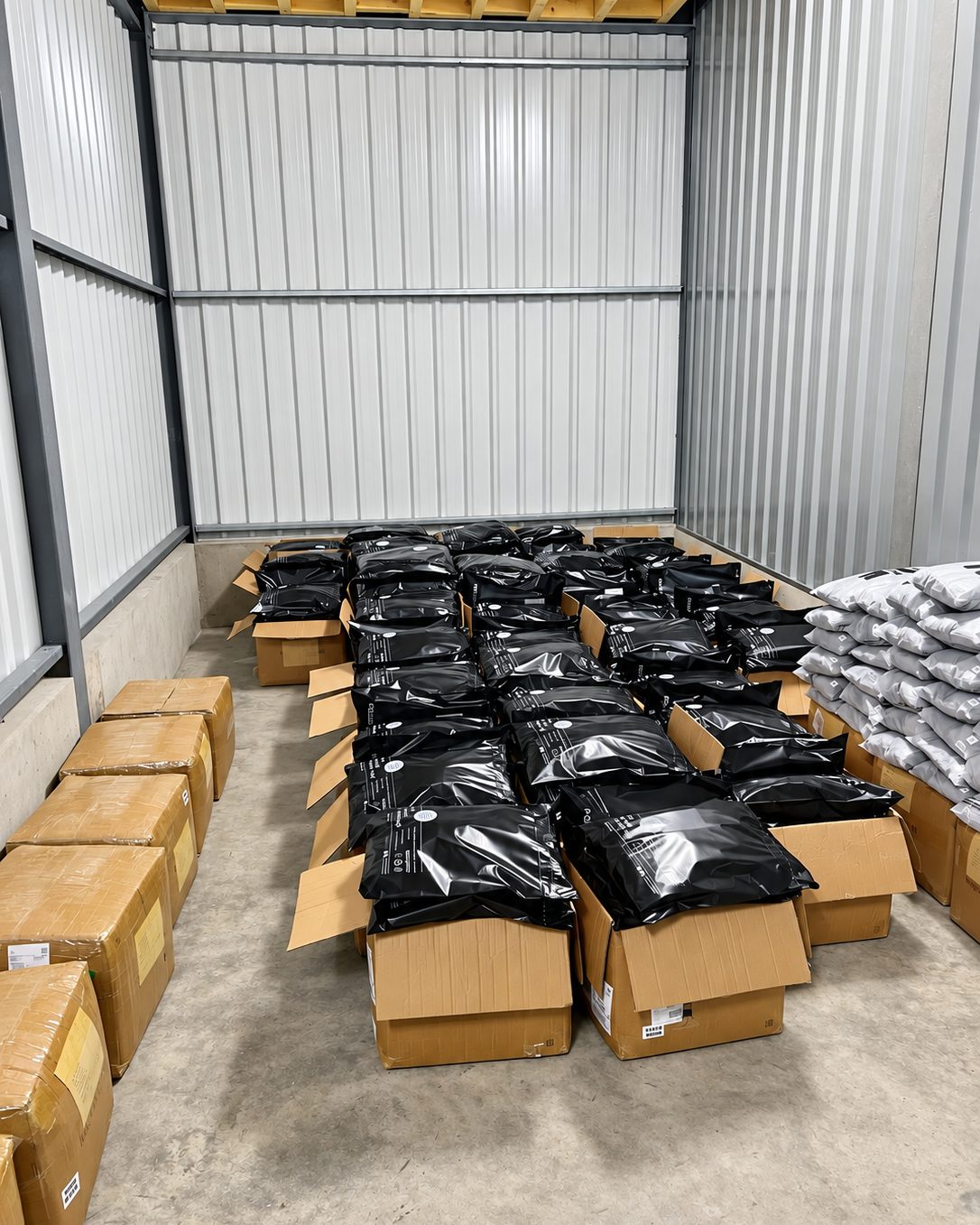 Lager mit offenen Kartons voller verpackter Bestellungen in schwarzen Versandbeuteln